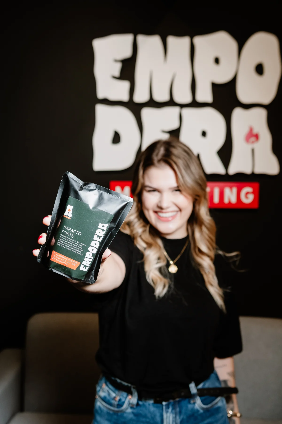 Maria apresentando o café da Empodera, com o logo da empresa ao fundo